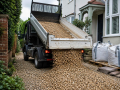 Small tipper vehicle delivering Aggregates in Eastbourne to a residential driveway with gravel and building materials on site.